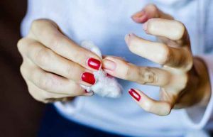 Young woman with long red nails removing nail polish