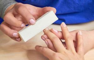 Manicurist polishing nails to client. Beautician filing nails for clients with buffing. Close up of female hands having manicure.
